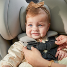 Baby in a car seat with harness being secured by an adult hand.