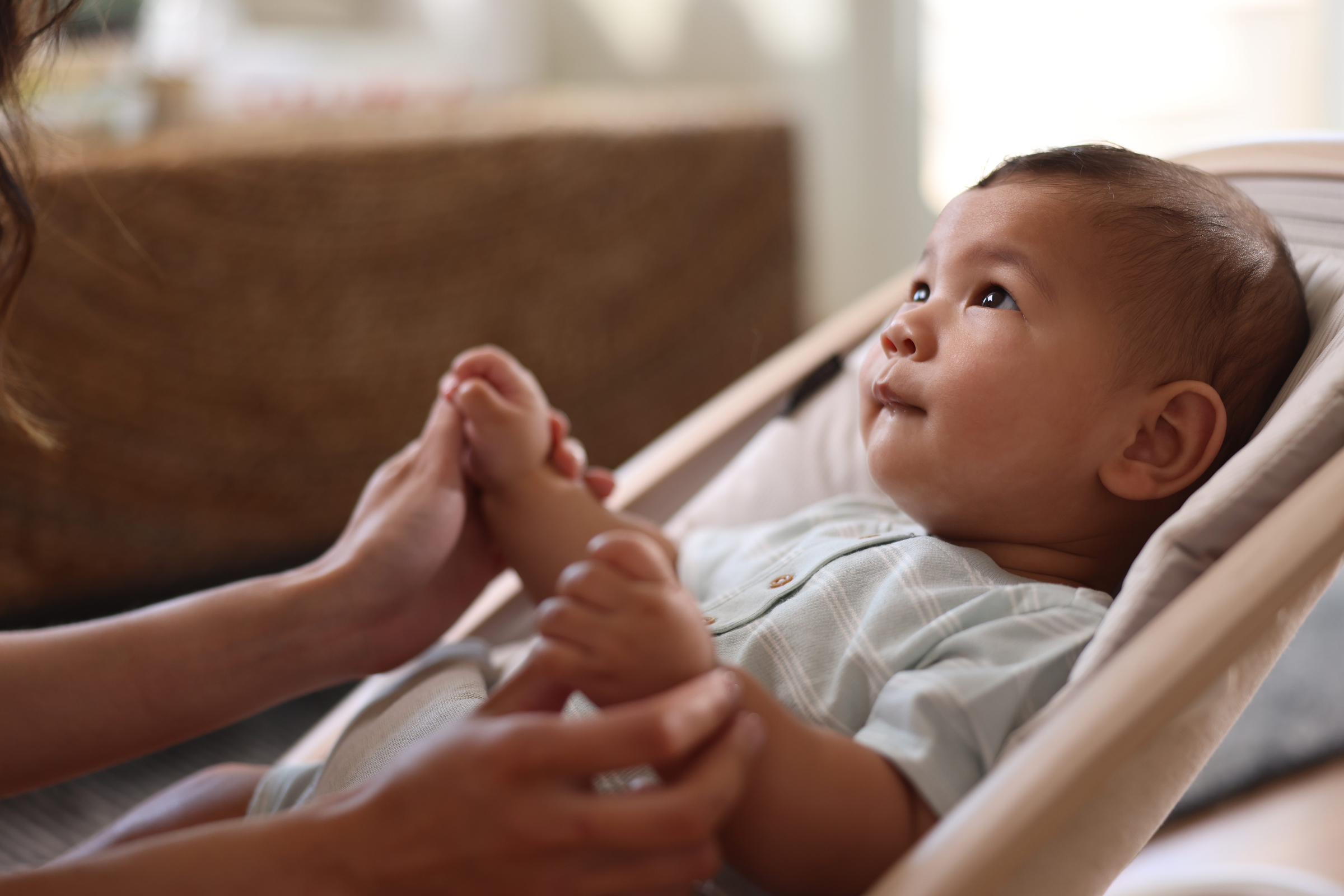 mother holding baby's hands while he rocks in Kori Rocker